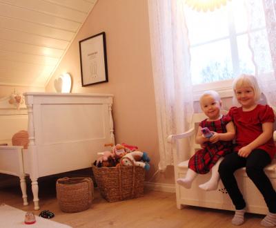 Två små flickor sitter på en säng i sitt rosa barnrum